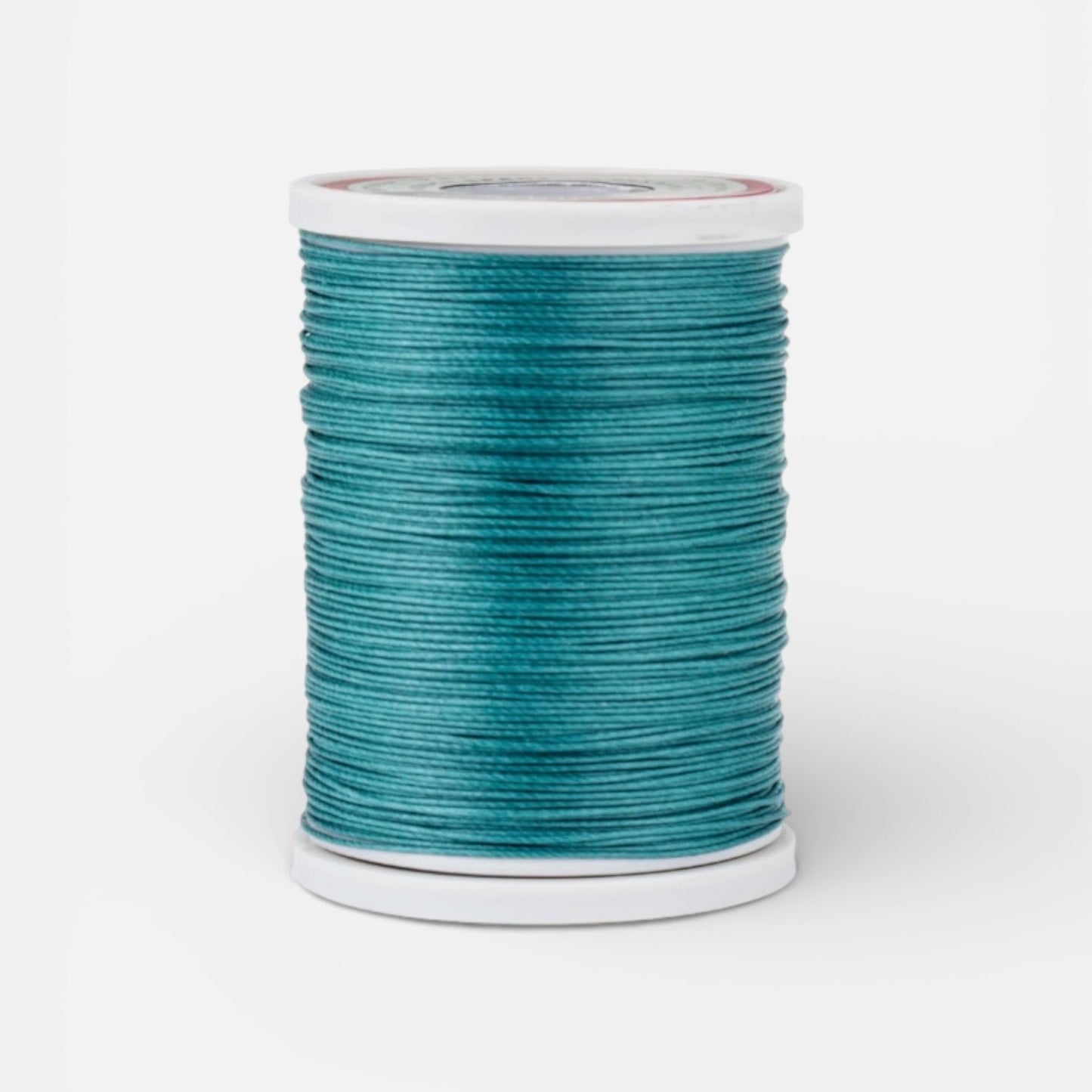 Spool of emerald teal thread for leathercraft on a light grey background