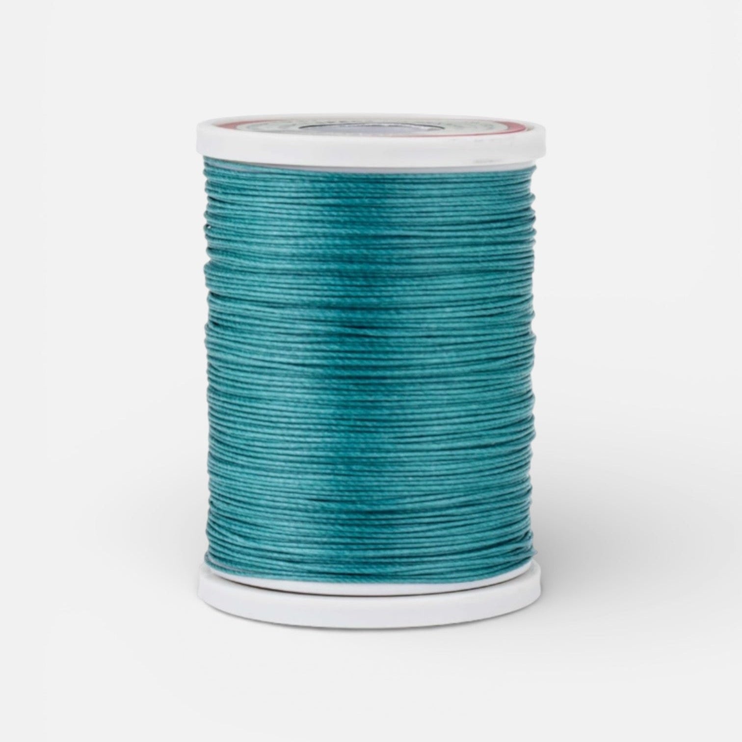 Spool of emerald teal thread for leathercraft on a light grey background
