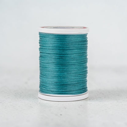 Spool of emerald teal thread for leathercraft on a light grey background