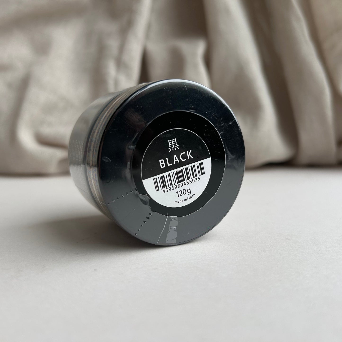 Black container of Tokonole with a label on a beige fabric background