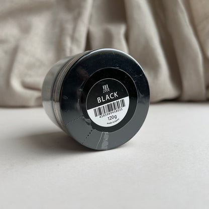 Black container of Tokonole with a label on a beige fabric background