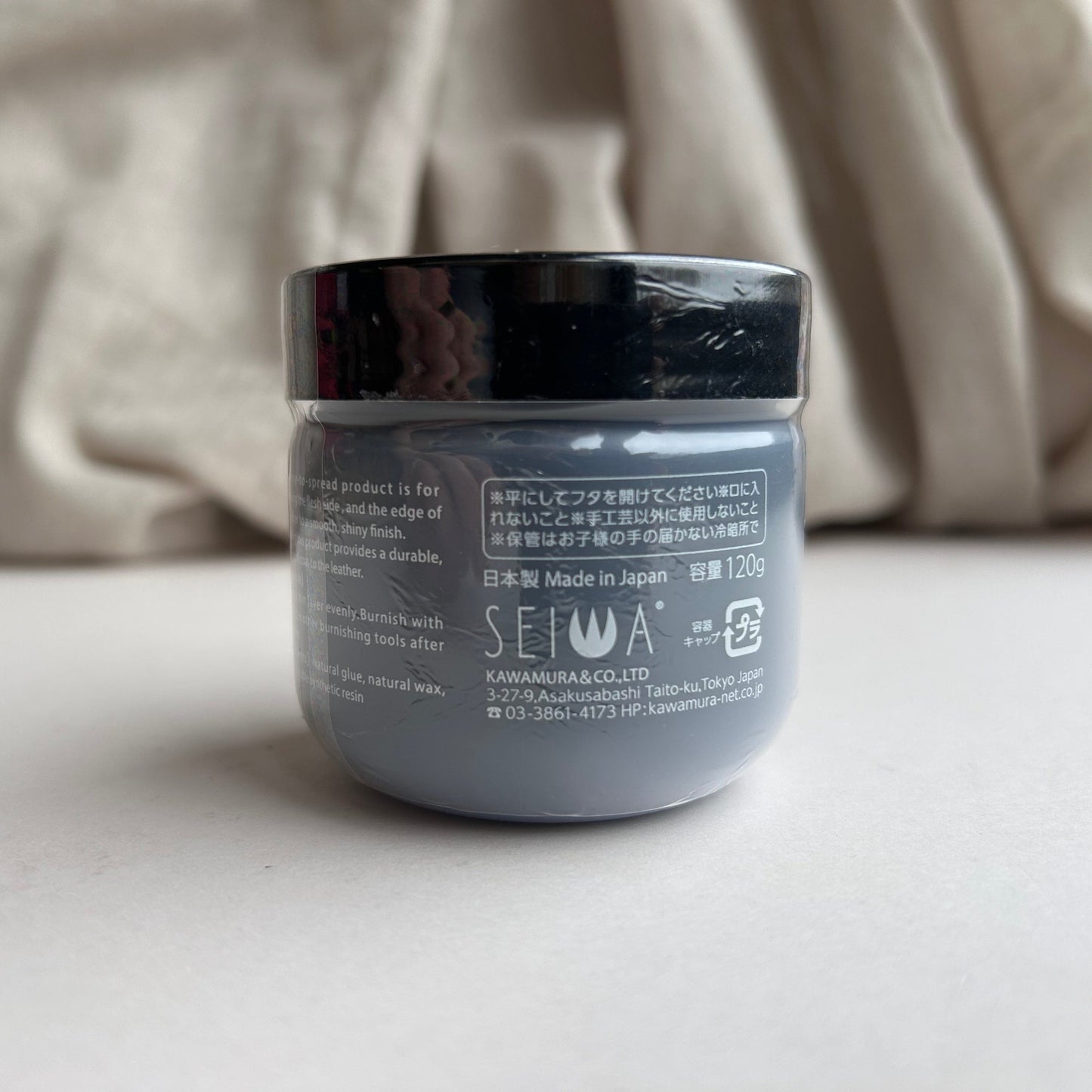 Jar of Tokonole with black lid on a light surface, blurred beige fabric in the background