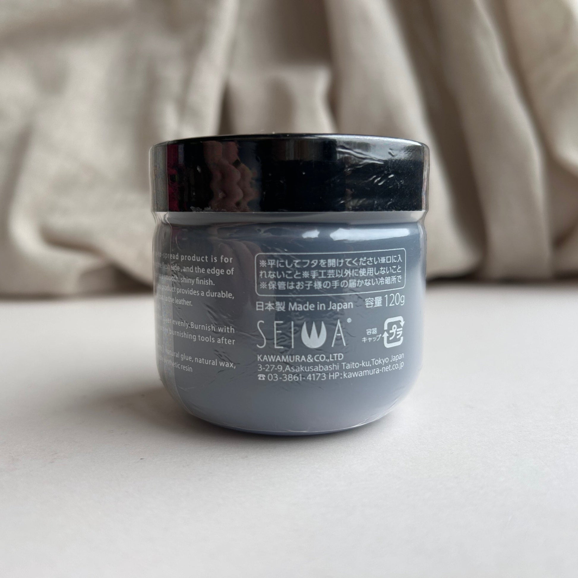 Jar of Tokonole with black lid on a light surface, blurred beige fabric in the background