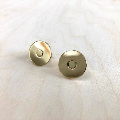 Gold magnetic snap fasteners on light wood background.