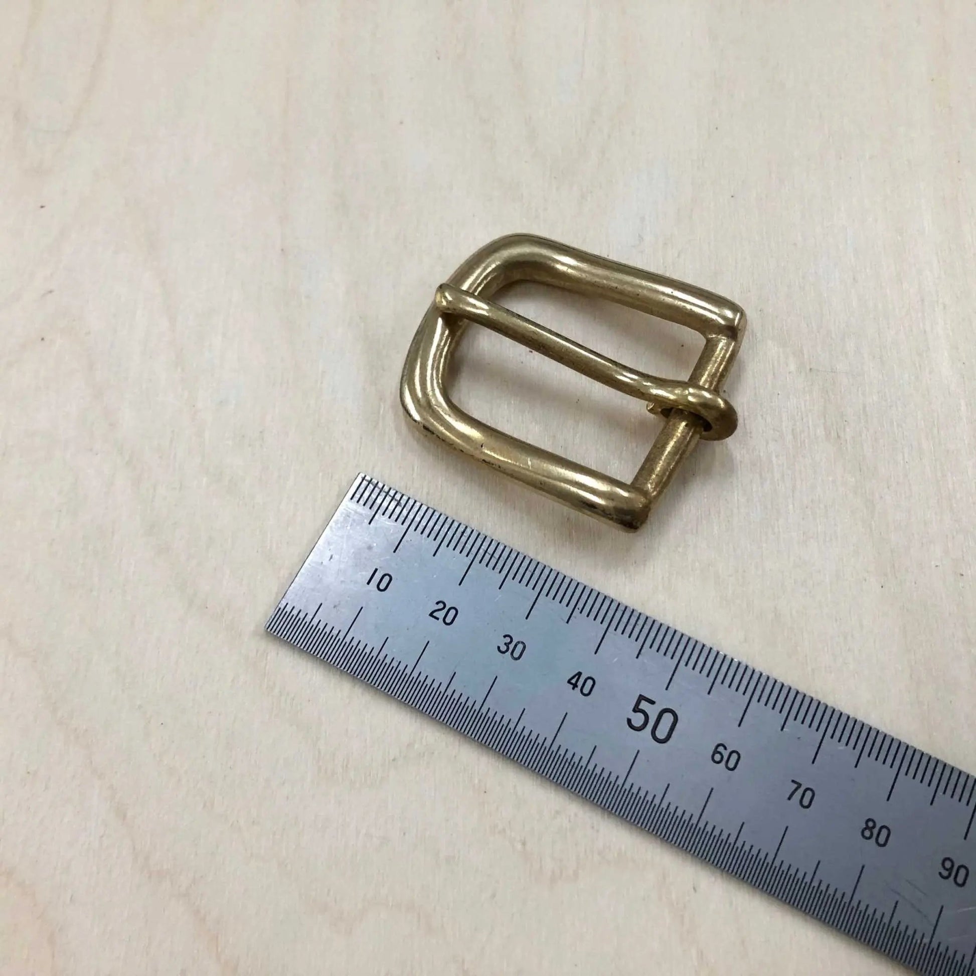 Solid Brass Buckle with rounded frame and pin on wooden surface with ruler for size reference.