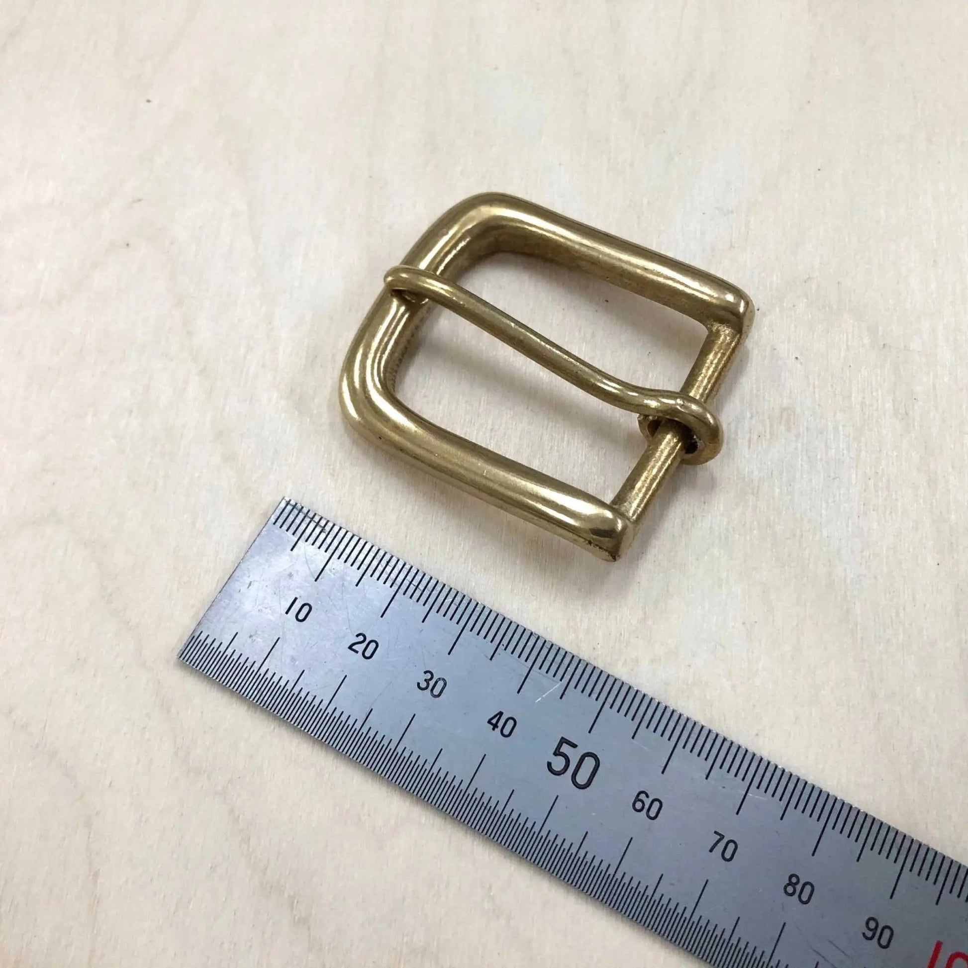 Solid brass buckle with rounded frame and pin, next to ruler for size reference.
